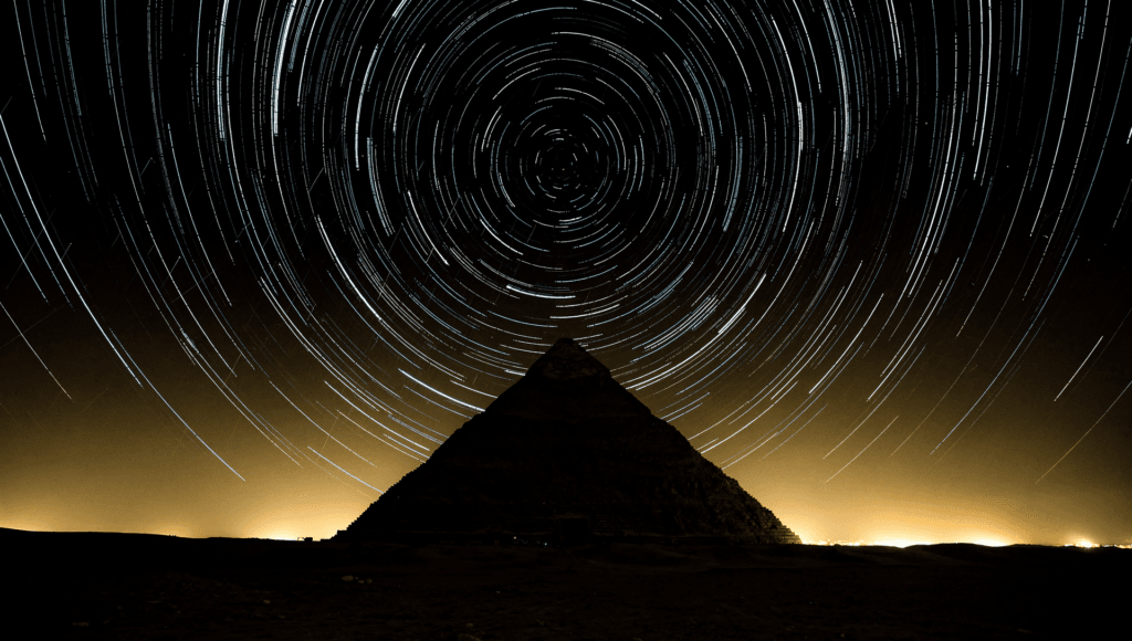 Pyramid under circling star trails and aurora, evoking the Pyramid Texts and the soul rising to the imperishable stars