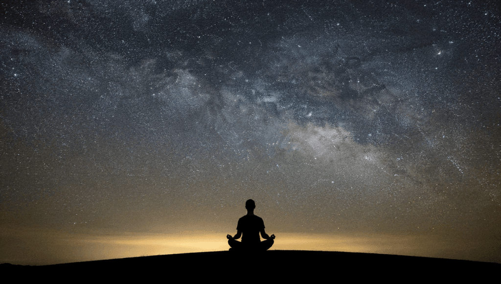 Supporting spiritual ascension: a person meditating on a hilltop beneath the Milky Way and aurora