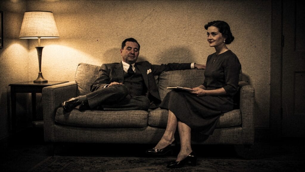 Illustration of a 1930s-style trance reading: a man resting with eyes closed while a woman sits beside him with a notebook